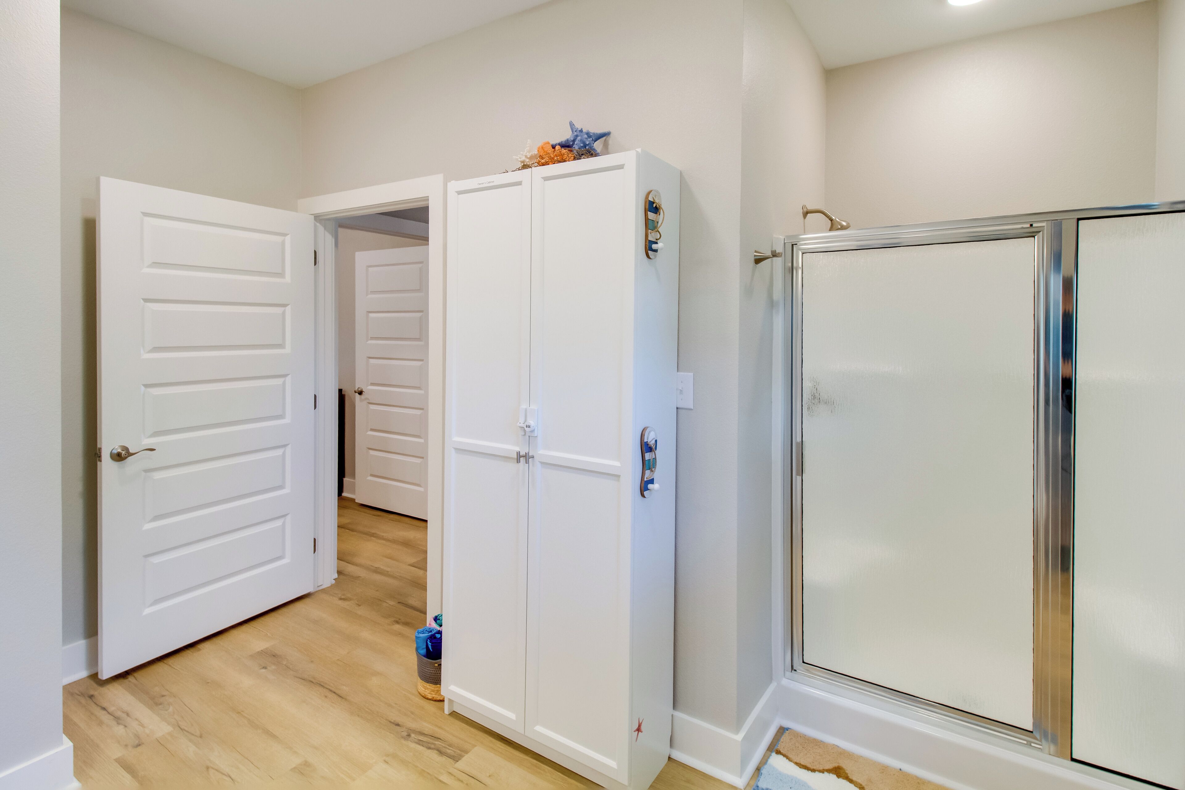 Un couloir avec une porte blanche, une armoire blanche et une cabine de douche en verre.