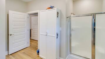 Un couloir avec une porte blanche, une armoire blanche et une cabine de douche en verre.