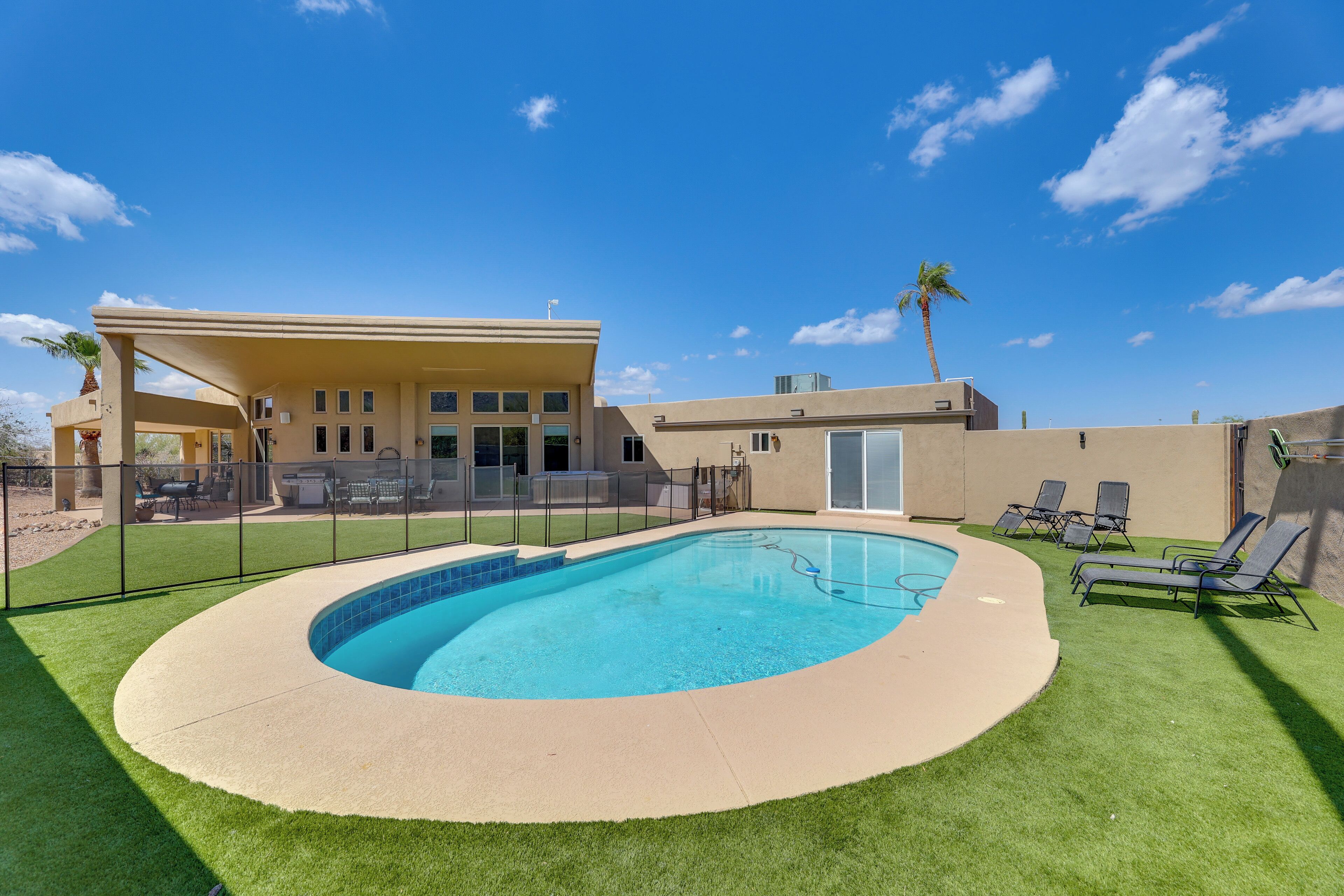 A swimming pool with a curved edge, surrounded by a beige deck and green artificial grass.