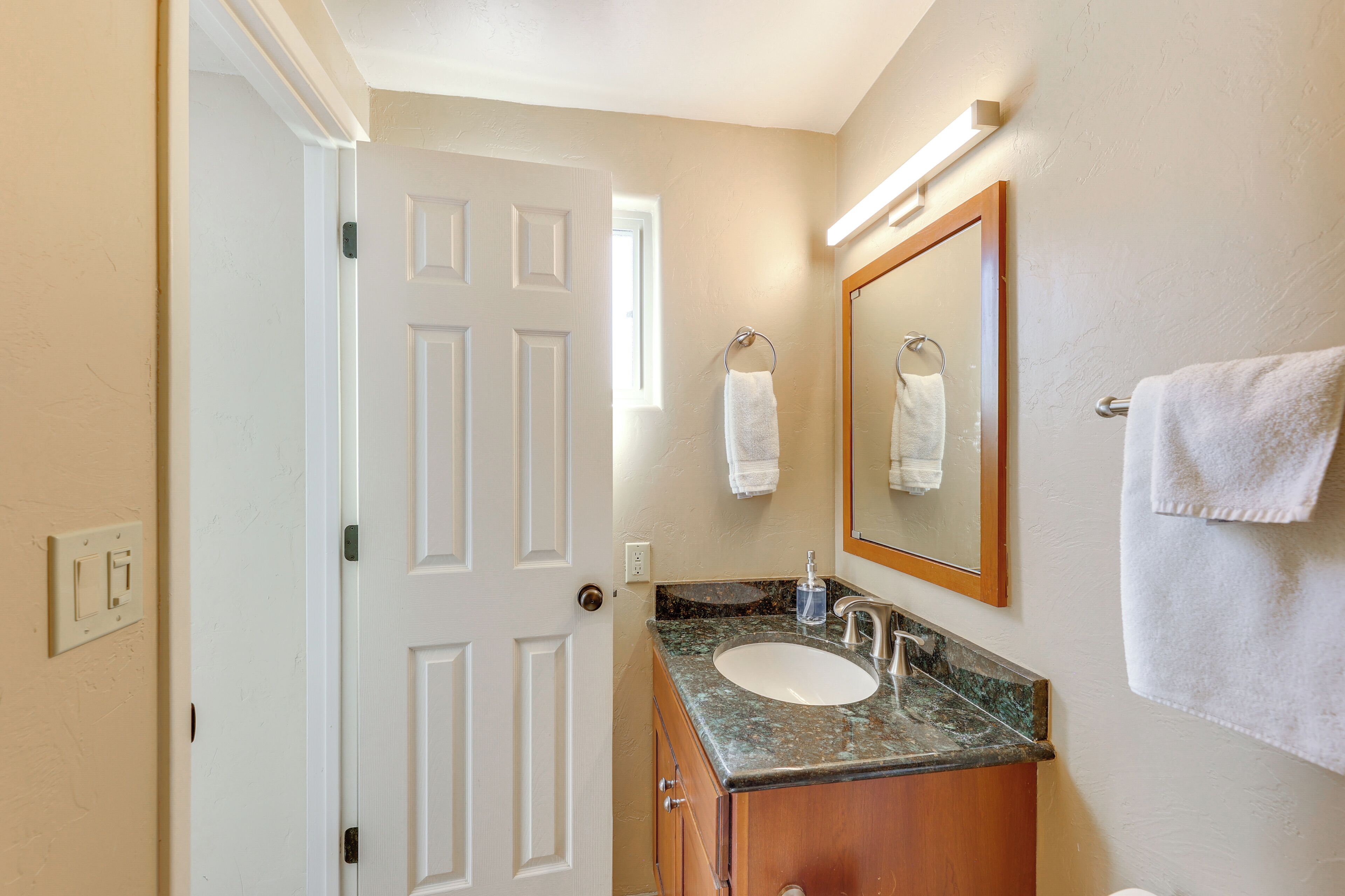 Une salle de bain avec une porte blanche, un lavabo doté d’un plan de travail en marbre, un miroir et une serviette accrochée au mur.