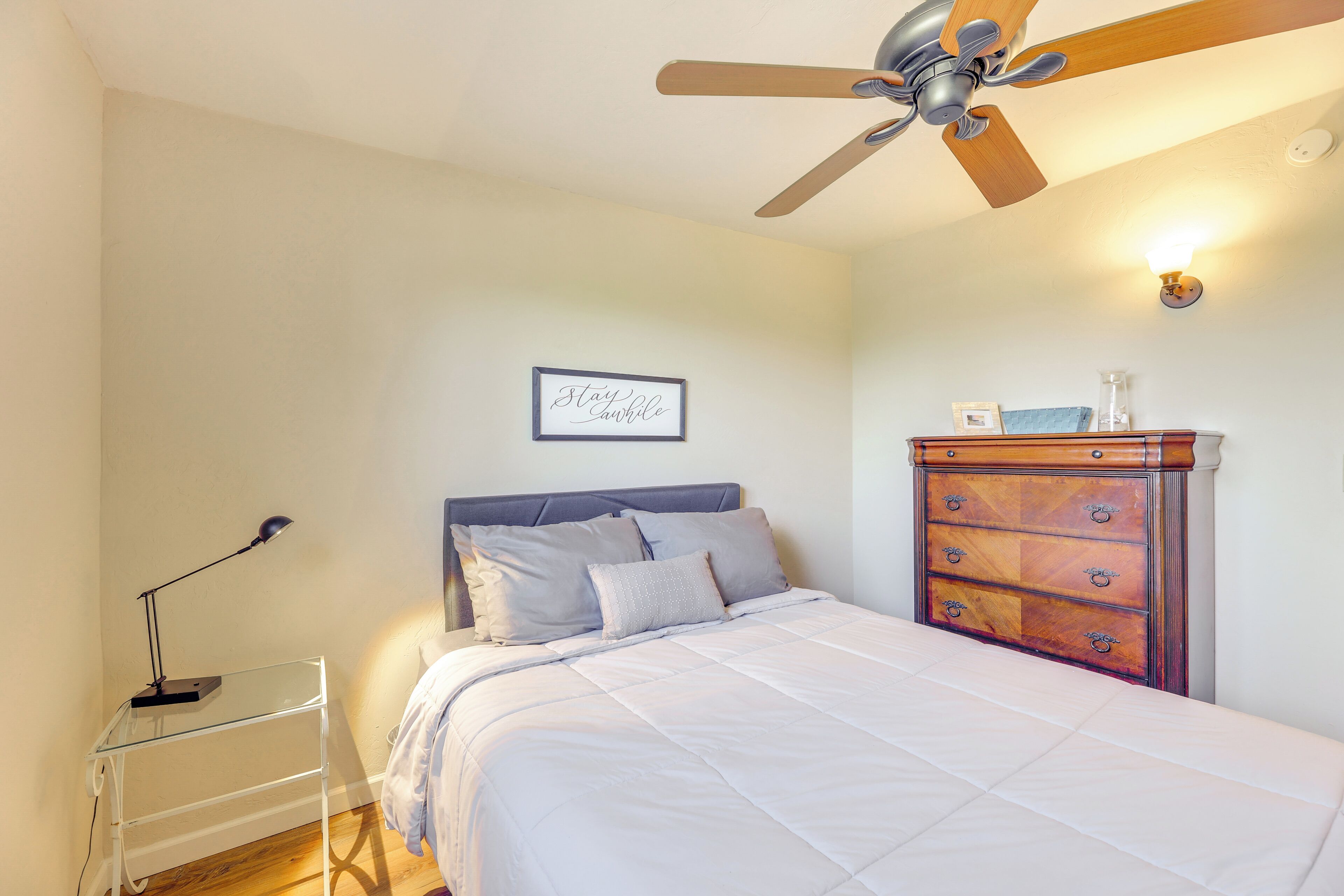 A bedroom with a bed, a dresser, a ceiling fan, a wall-mounted light, and a framed quote on the wall.