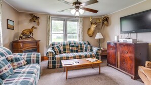 A living room with a plaid sofa, a wooden coffee table, a television, and mounted animal heads on the wall. - Pet-friendly Smithmill Retreat w/ Yard! (Houtzdale)