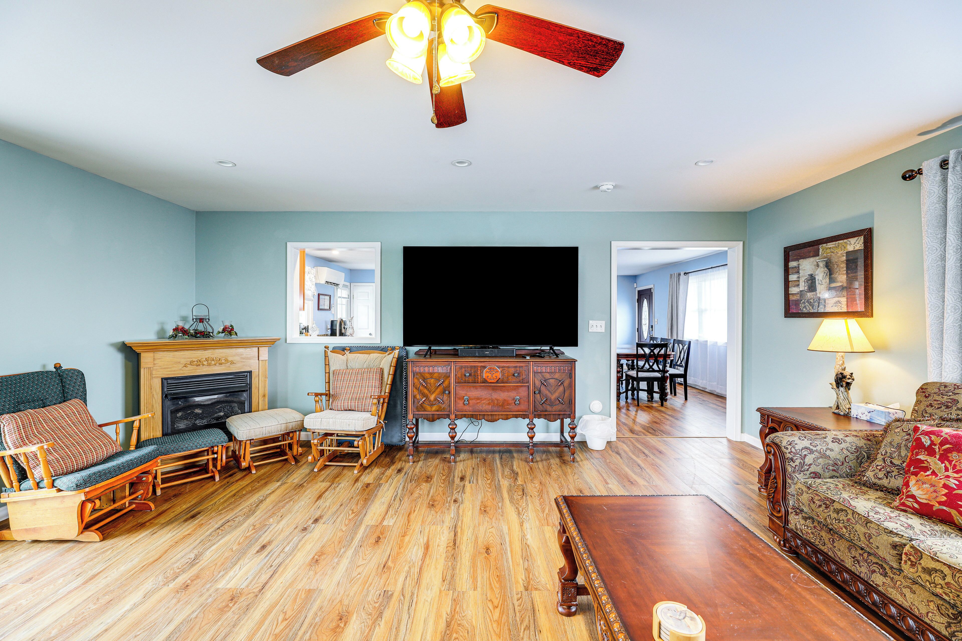 A living room with a fireplace, wooden furniture, a ceiling fan, and a television.