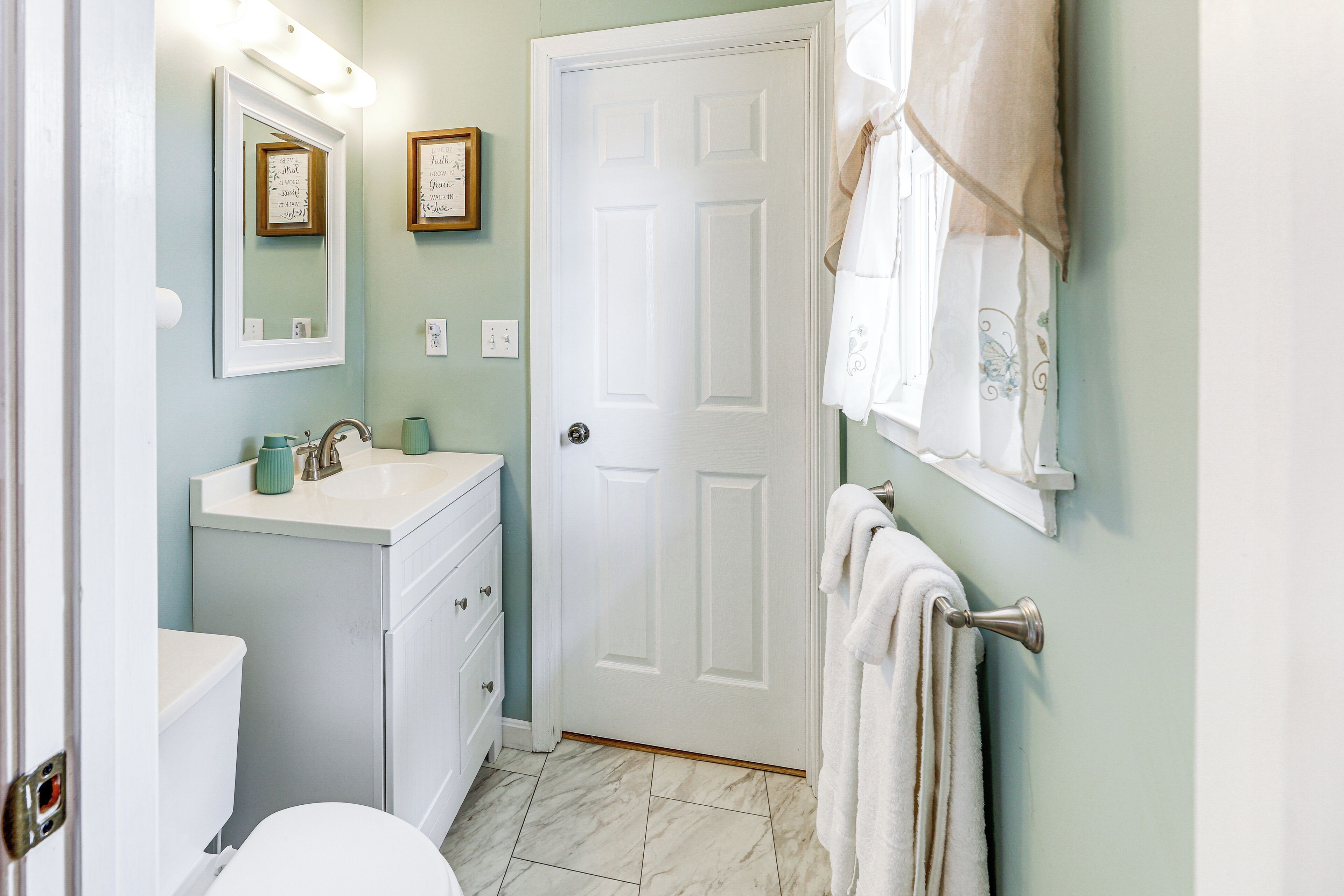 A bathroom with a white toilet, a sink with a mirror above it, and a towel hanging on a rack.