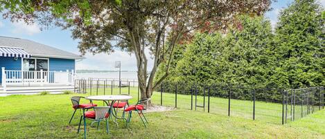 A grassy area with a table and chairs, a fenced garden, and a building with a blue exterior.