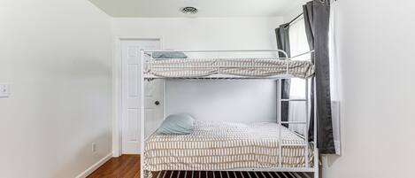 Una cama litera en una habitación con paredes blancas y suelo de madera.