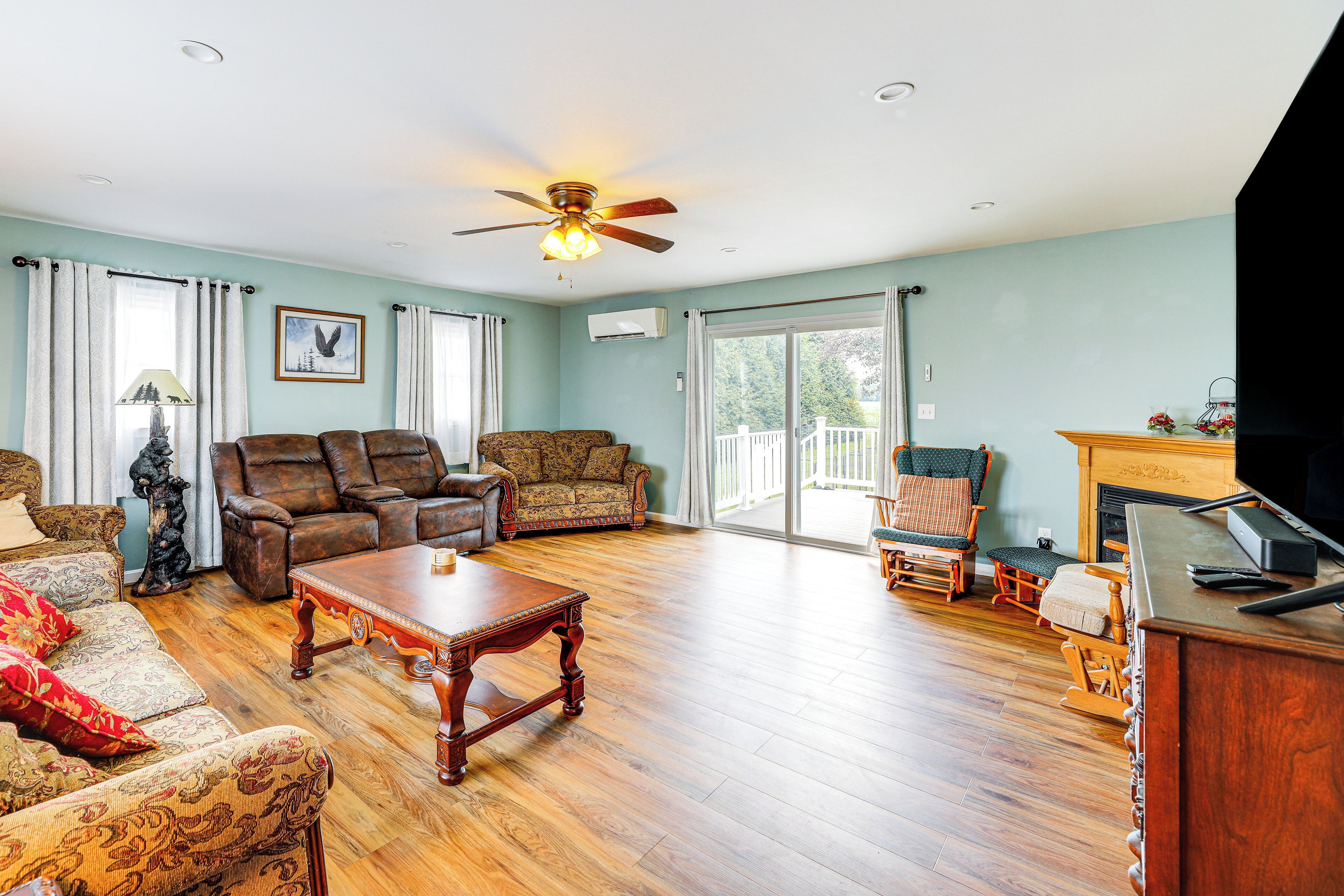 A spacious living room with a wooden floor, leather sofas, a wooden coffee table, and a ceiling fan.