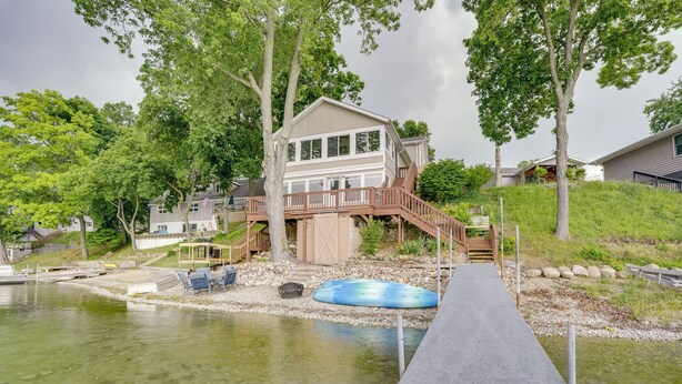 A house with a dock extending into a lake, surrounded by trees and a grassy hill. - Game Room & Outdoor Fun - Gilead Lake Getaway! (Bronson)