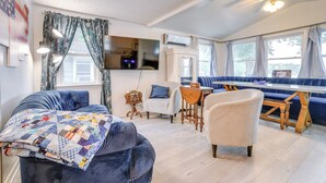 Una sala de estar acogedora con un sofá azul, un sillón blanco y una zona de comedor con un banco azul.