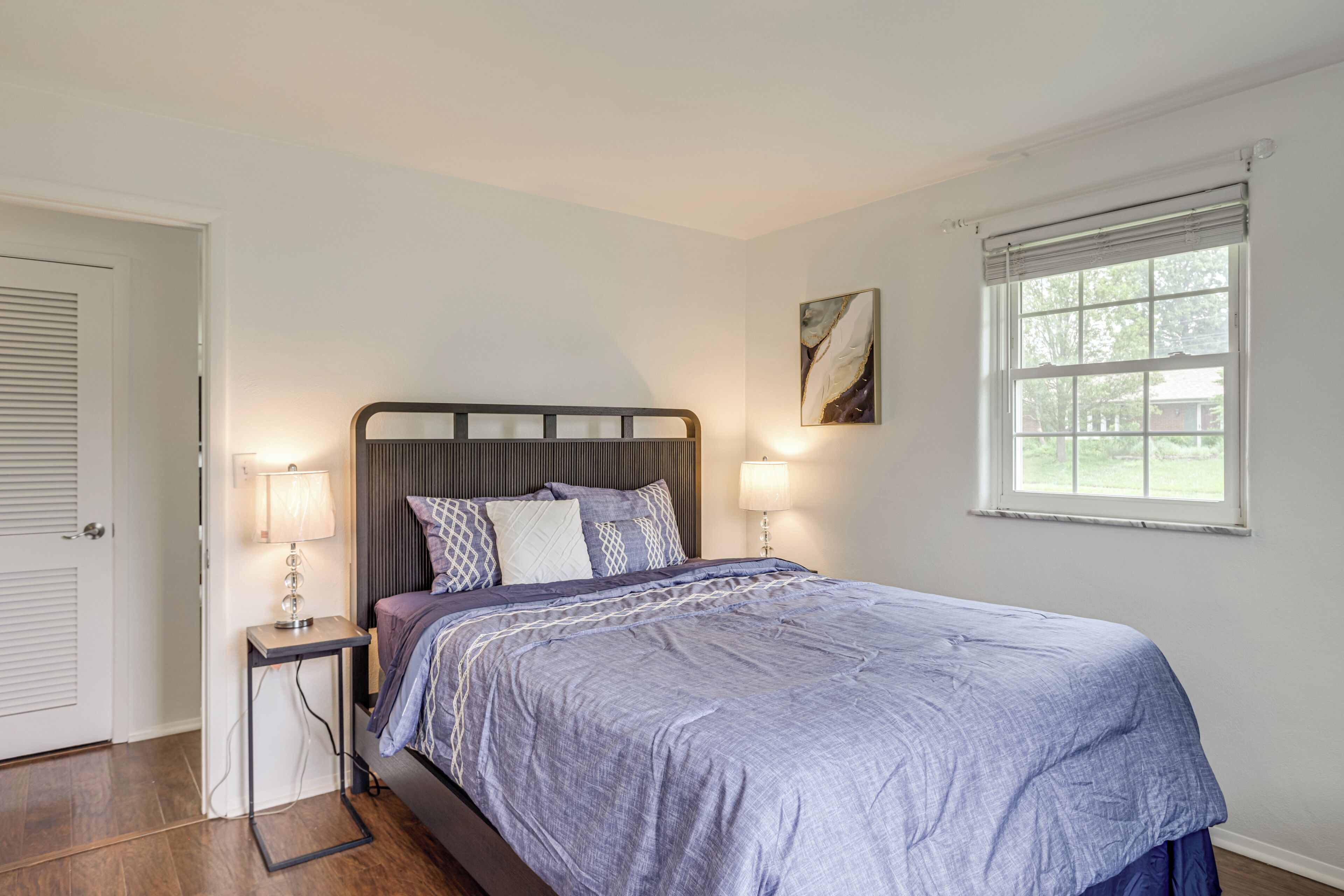 A bedroom with a bed, bedside lamps, a window, and a door.