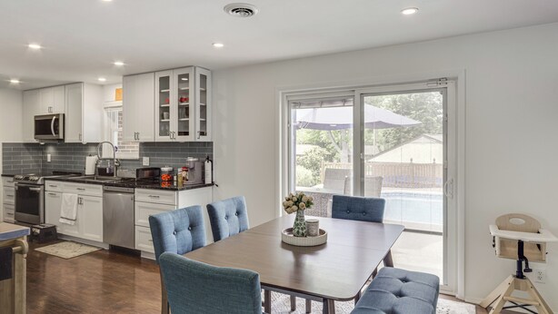 A modern kitchen with white cabinets, a dining area with blue chairs, and a large window with a view of the outdoors. - Dayton Family Home w/ Game Room: Walk to City Park (Dayton)