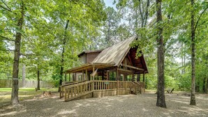 Een rustieke chalet met een houten terras en een overdekte veranda, omringd door bomen.
