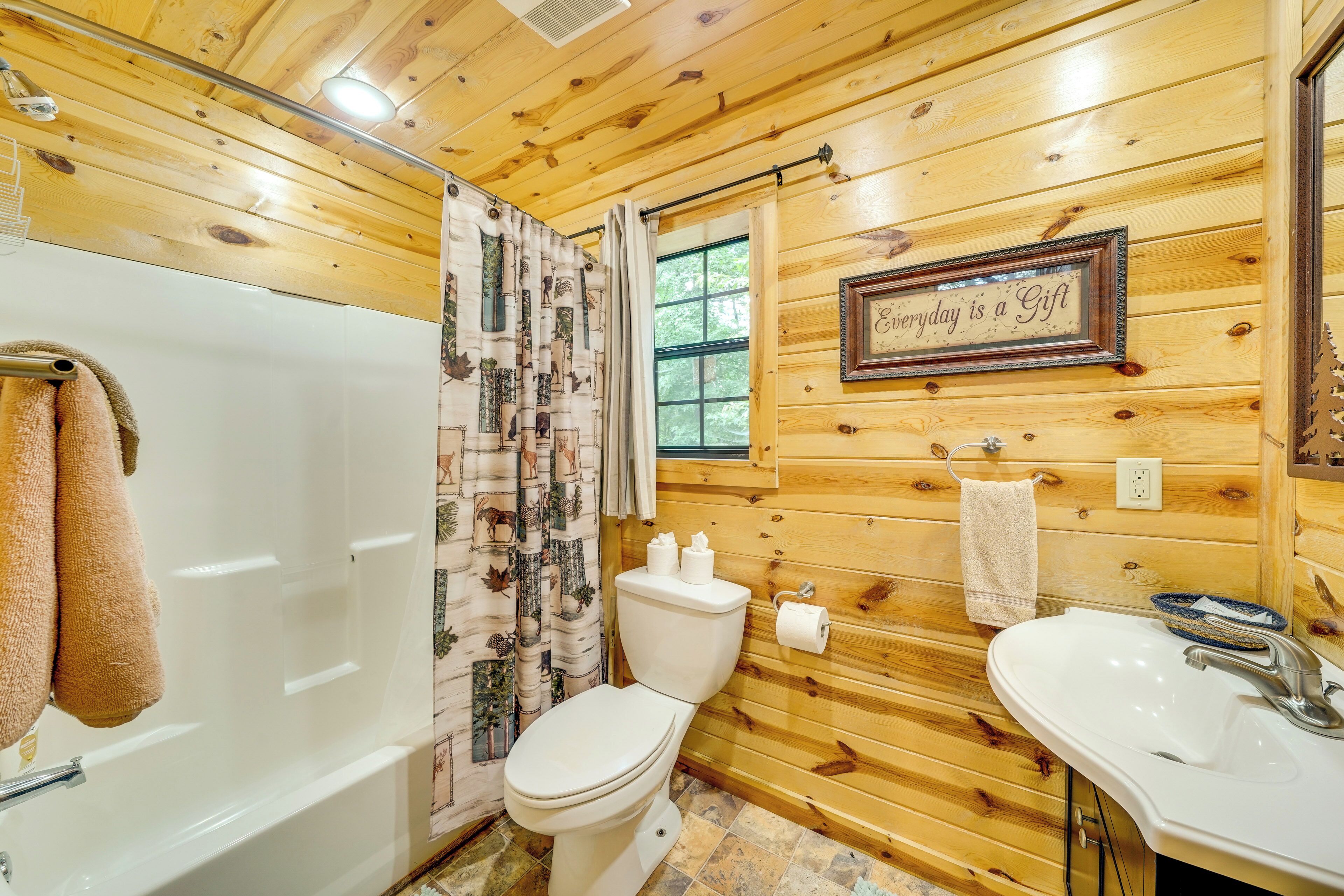 A wooden cabin bathroom with a bathtub, toilet, and sink.