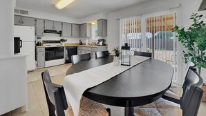 Una cocina moderna con armarios grises, un comedor con mesa negra y un ventanal con persianas.