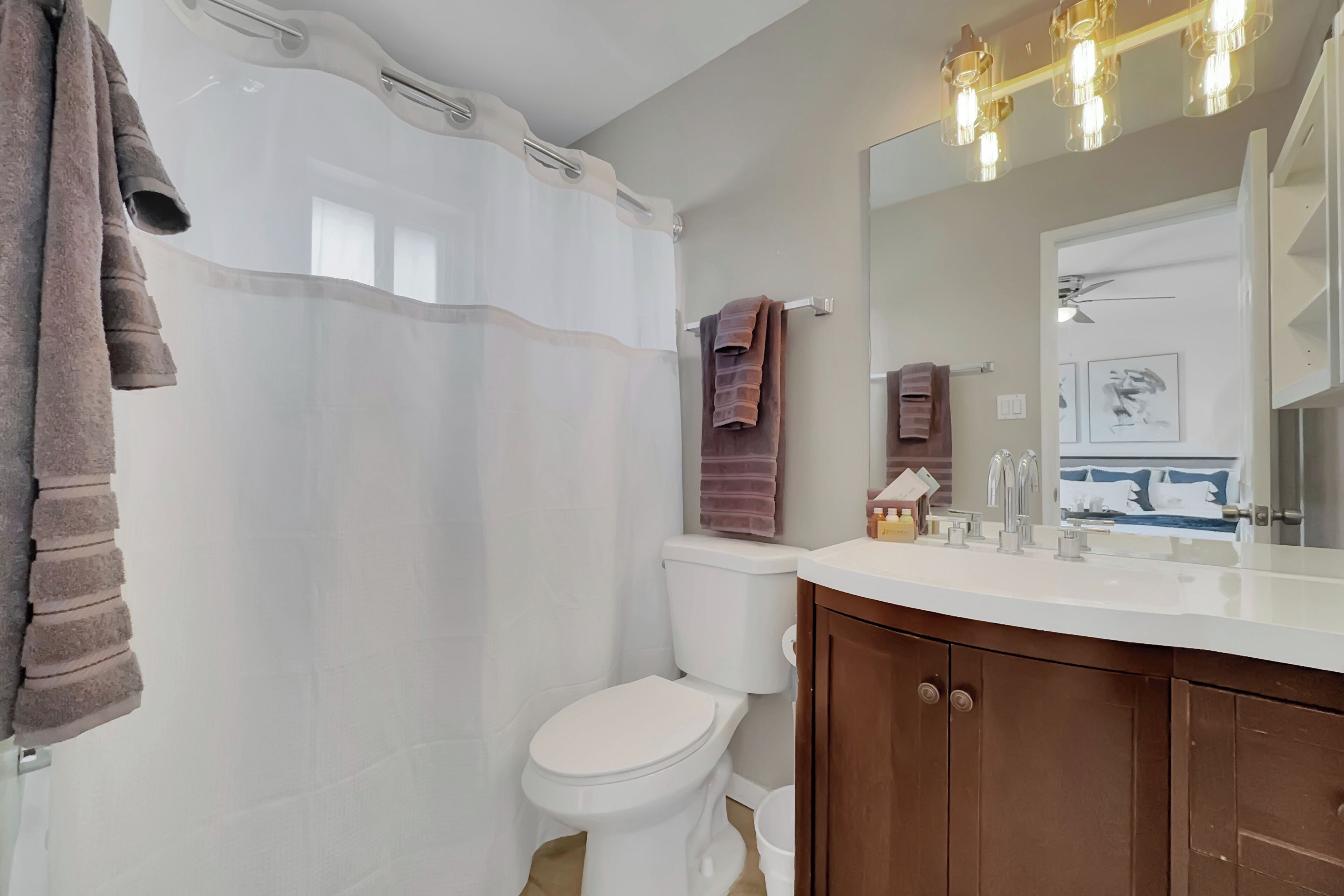 A bathroom with a white toilet, a shower curtain, a vanity with a mirror, and a towel rack.