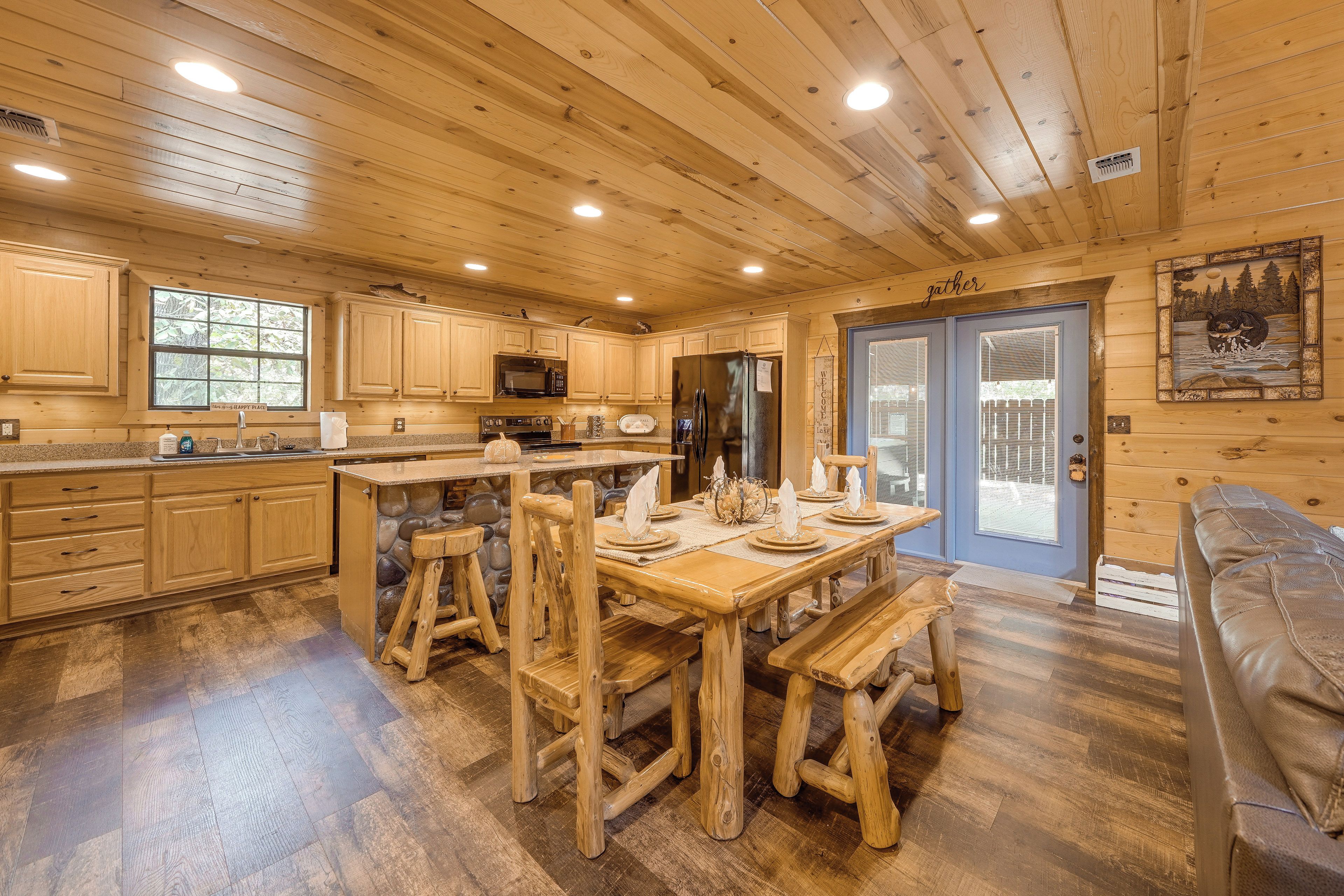 A wooden cabin interior with a kitchen, dining area, and a stone wall feature.