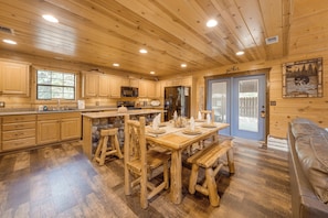 A wooden cabin interior with a kitchen, dining area, and a stone wall feature. - Near Choctaw Landing 2 King Bedrooms Game Loft (Broken Bow)