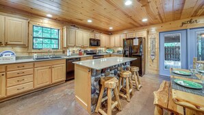 A spacious kitchen with wooden cabinets, a granite countertop, a stone island with stools, and a large window. - Near Choctaw Landing 2 King Bedrooms Game Loft (Broken Bow)