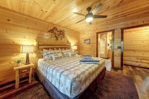 Une pièce chaleureuse en bois, avec un lit, une table de chevet, un ventilateur de plafond et une porte.