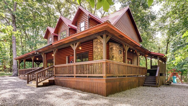 A rustic cabin with a stone foundation, wooden deck, and a red roof. - Near Choctaw Landing 2 King Bedrooms Game Loft (Broken Bow)