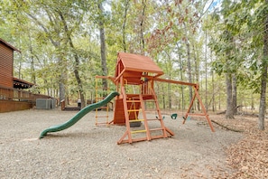 A wooden play structure with a slide and swings in a wooded area. - Near Choctaw Landing 2 King Bedrooms Game Loft (Broken Bow)