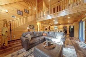 A spacious living area with a large leather sectional sofa, a wooden staircase, and a kitchen in the background. - Near Choctaw Landing 2 King Bedrooms Game Loft (Broken Bow)