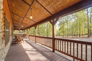 Une terrasse en bois couverte, dotée de fauteuils à bascule, d’un mur en pierre et offrant une vue sur une forêt.