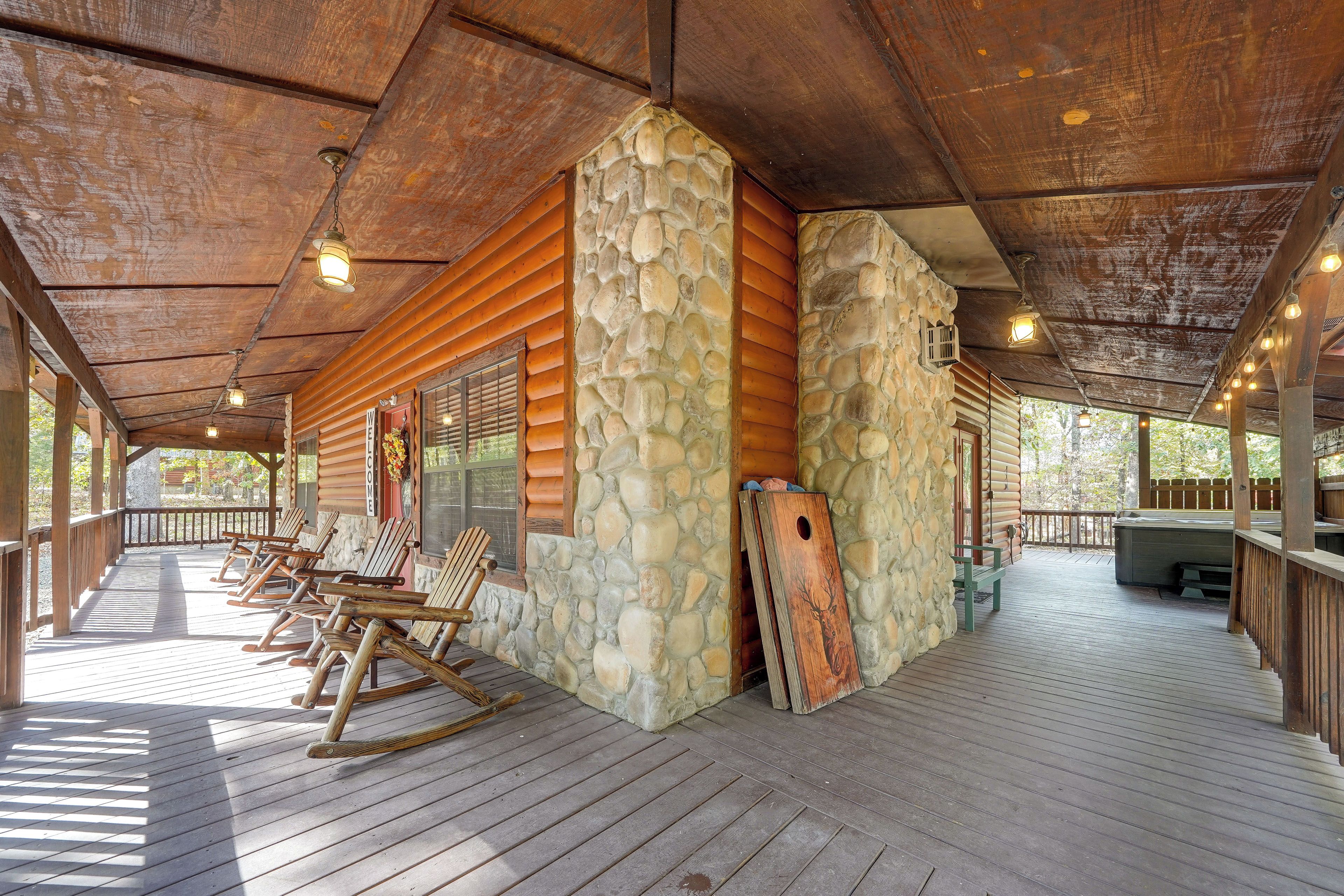 A covered outdoor area with wooden flooring, stone walls, and a wooden deck with chairs.