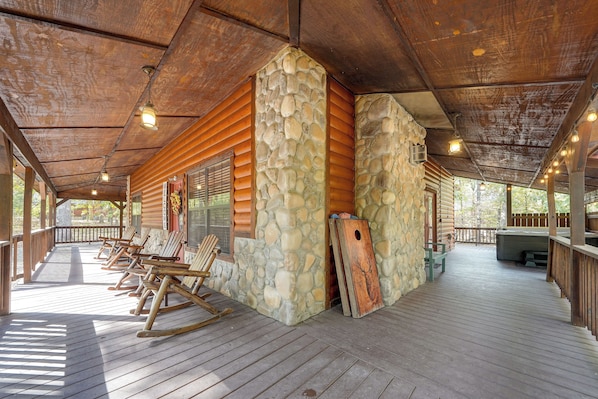 A covered outdoor area with wooden flooring, stone walls, and a wooden deck with chairs. - Near Choctaw Landing 2 King Bedrooms Game Loft (Broken Bow)