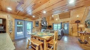A wooden cabin interior with a dining area, a stone fireplace, and a view of the outdoors. - Near Choctaw Landing 2 King Bedrooms Game Loft (Broken Bow)
