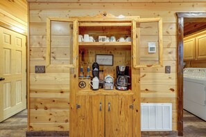 Un meuble en bois contenant une machine à café et des tasses, une pancarte indiquant « C’est l’heure du café », et un petit égouttoir à vaisselle.
