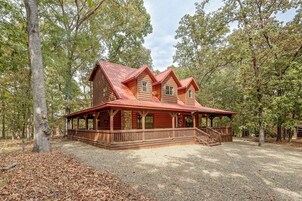 A wooden cabin with a porch and a stone wall, surrounded by trees.