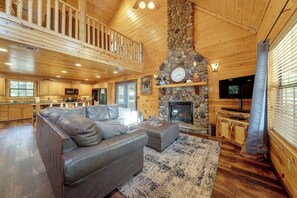 A spacious living room with a stone fireplace, a large sofa, and a television. - Near Choctaw Landing 2 King Bedrooms Game Loft (Broken Bow)