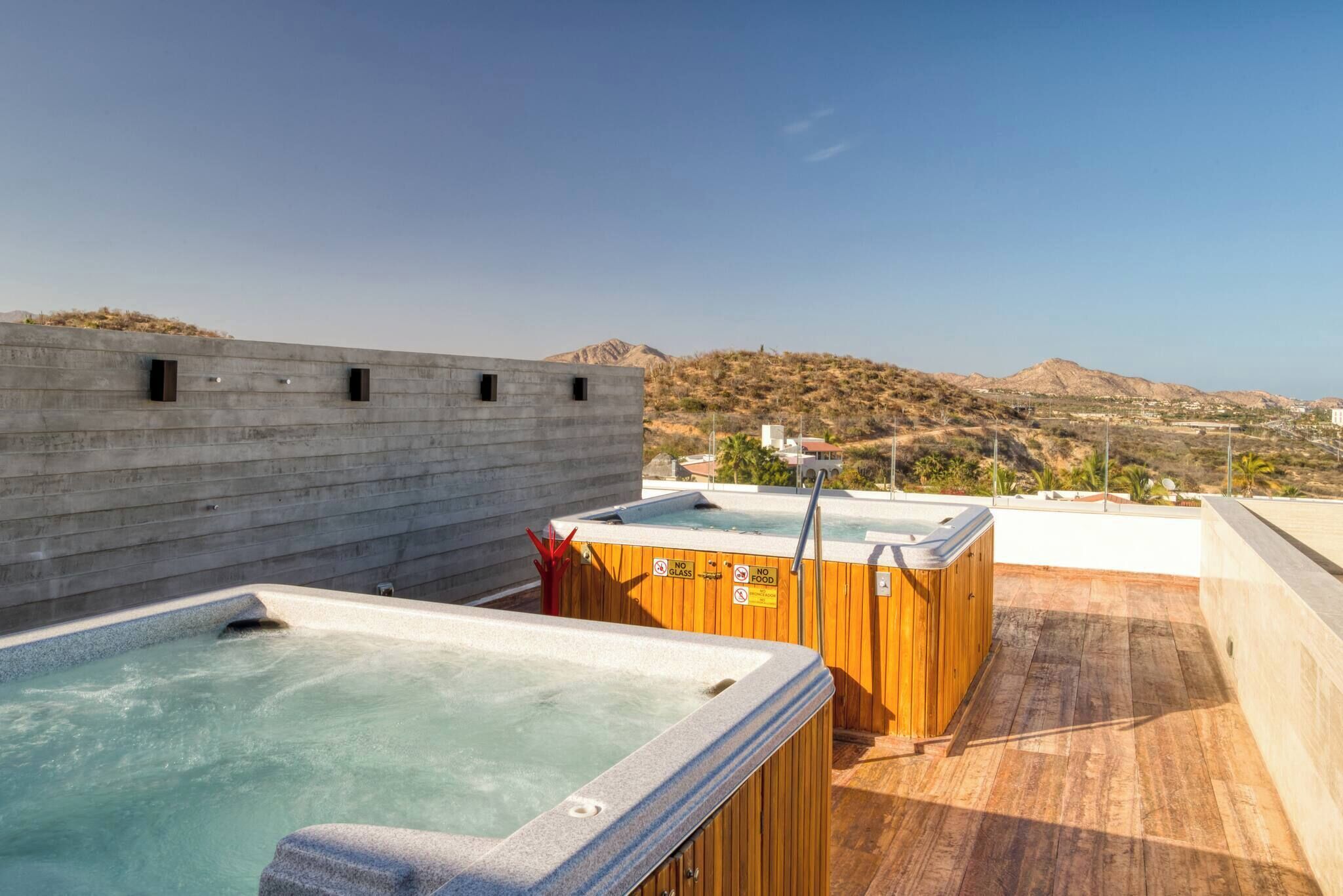 Una azotea con dos jacuzzis, una terraza de madera y vistas a un paisaje montañoso.