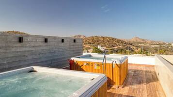 Una azotea con dos jacuzzis, una terraza de madera y vistas a un paisaje montañoso.