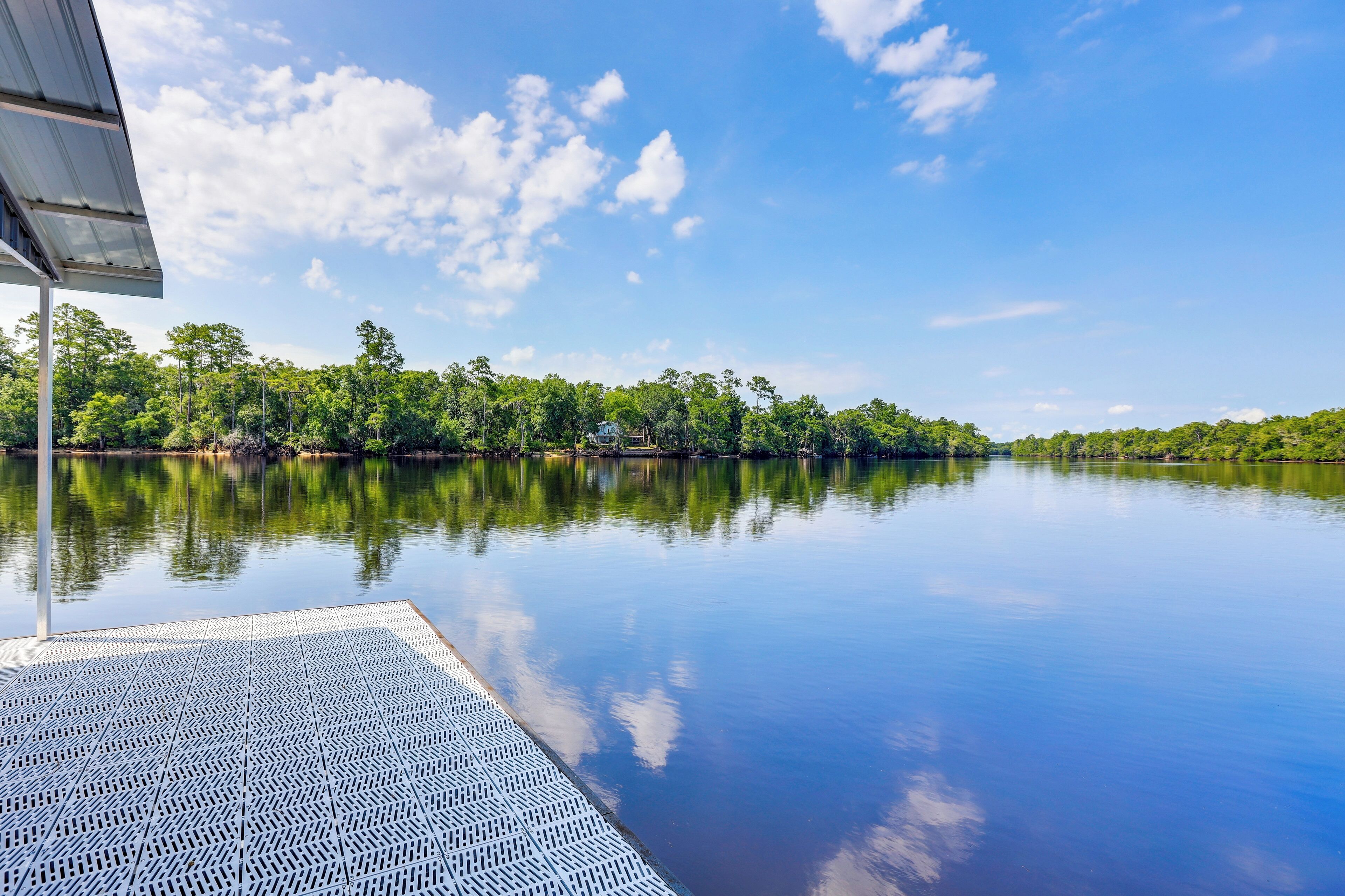 A calm lake with a dock extending into the water, surrounded by dense trees and a clear sky.