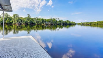 A calm lake with a dock extending into the water, surrounded by dense trees and a clear sky.