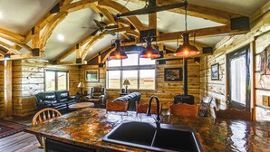 Interior d'una cabana rústica amb una zona de menjador de fusta, una cuina illa gran amb un rentaplat i un ventilador de sostre.