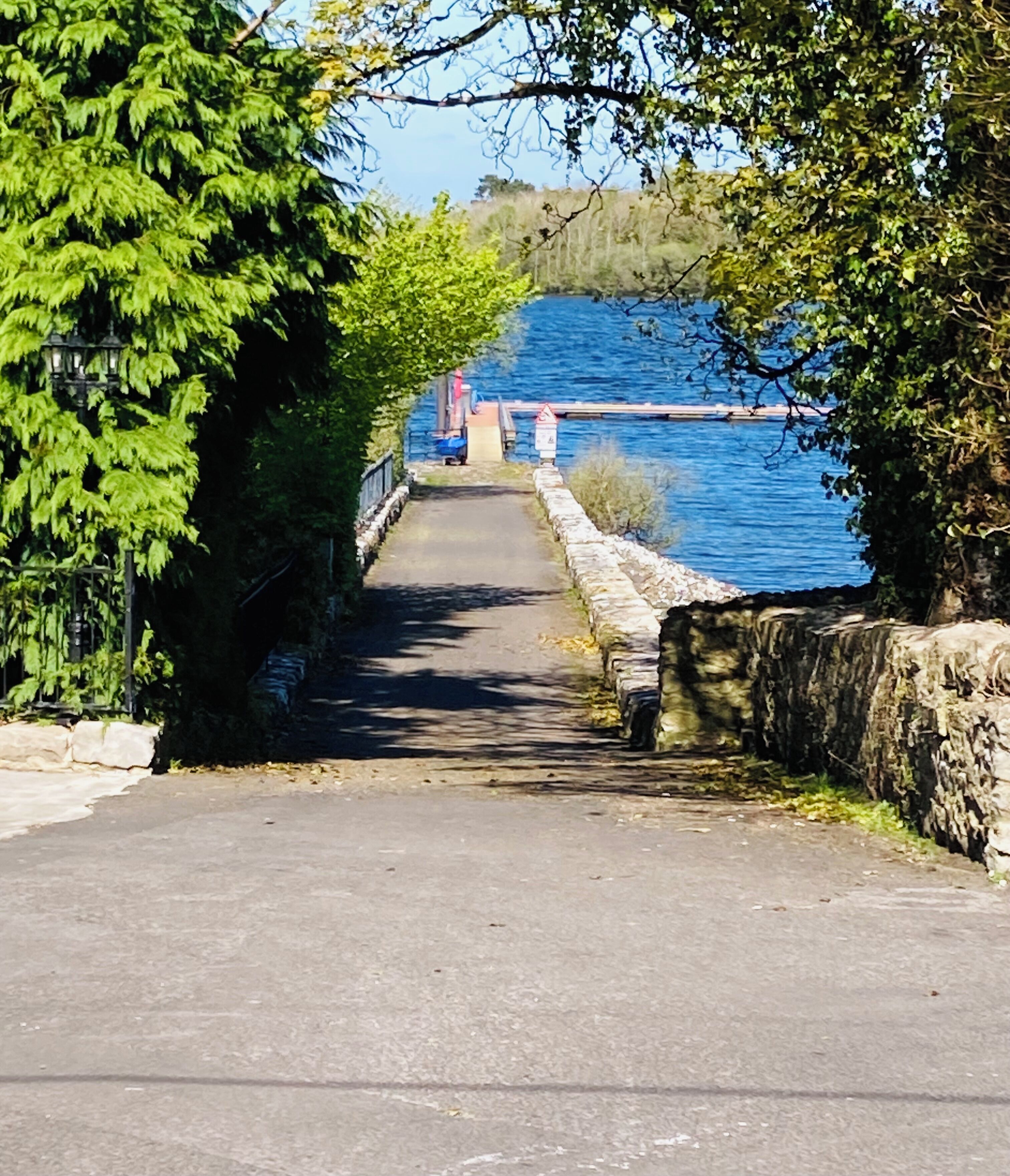 A pathway leading to a dock over a body of water, surrounded by trees and stone walls.