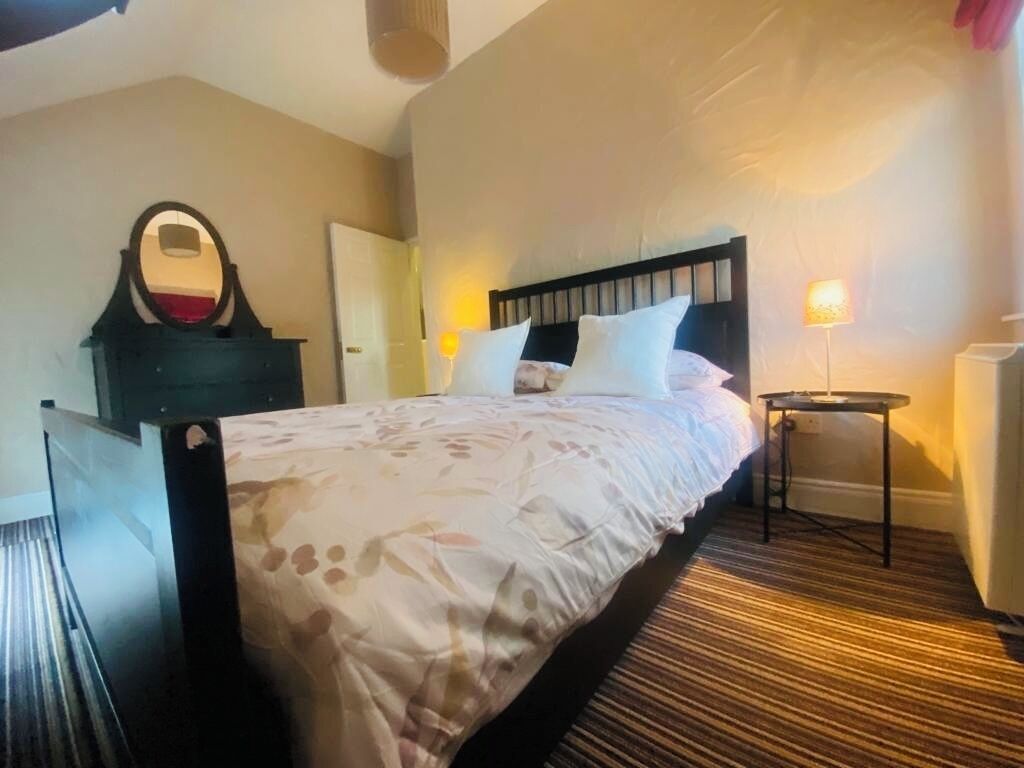 A hotel room with a bed, a bedside table, a lamp, and a mirror.