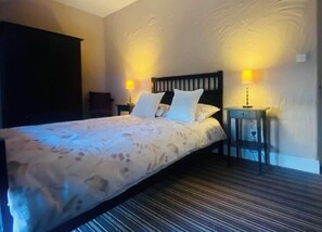 A neatly made bed with a floral bedspread, two bedside lamps, a dark wooden headboard, and a striped carpet. - The Old Boathouse Holiday Cottage on the Shores of Lough Erne-4 Double Bedrooms (Derrylin Enniskillen)