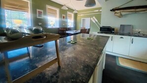Une cuisine avec un plan de travail foncé, des armoires blanches et des luminaires suspendus.