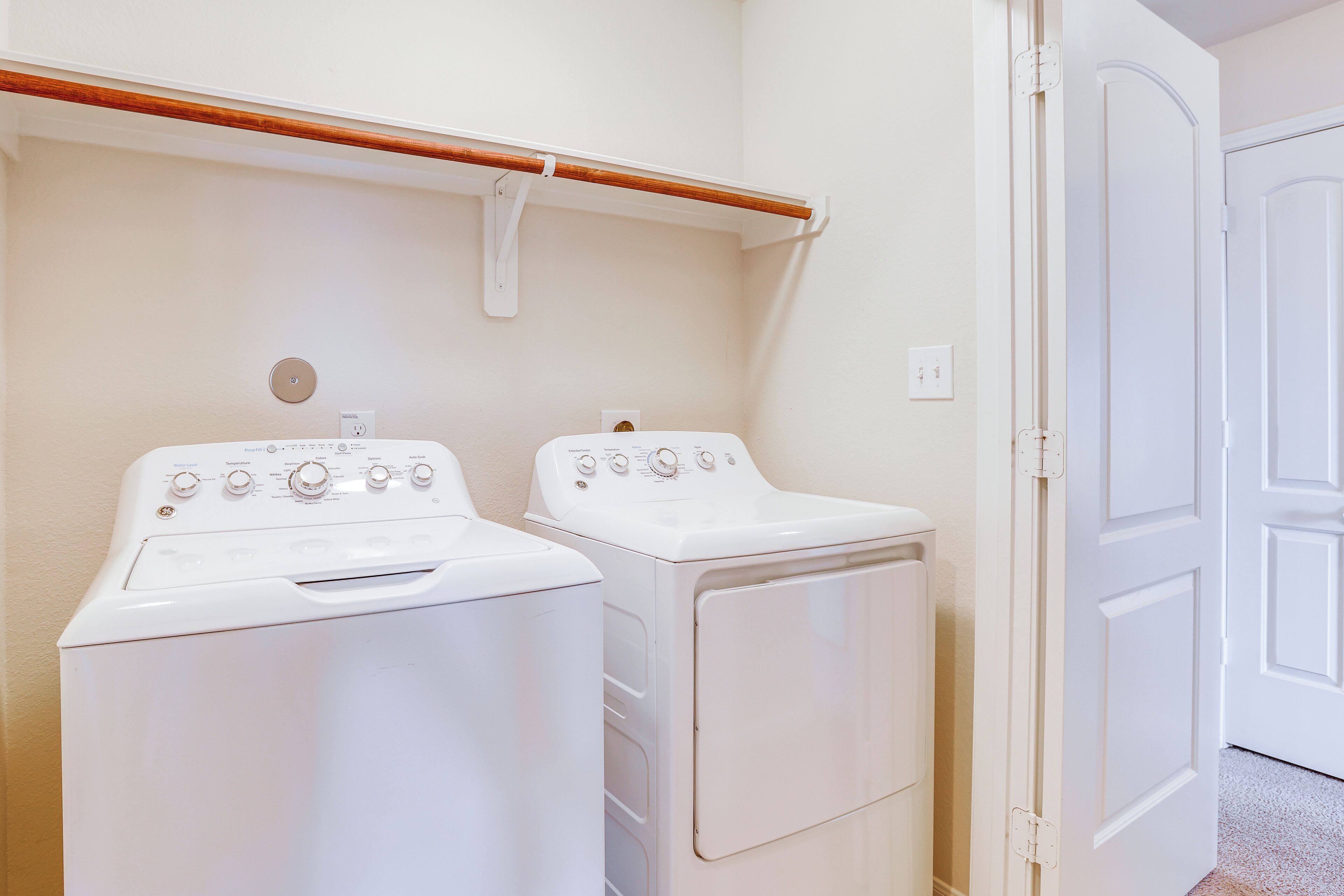 A laundry room with two white washing machines and a wooden drying rack.