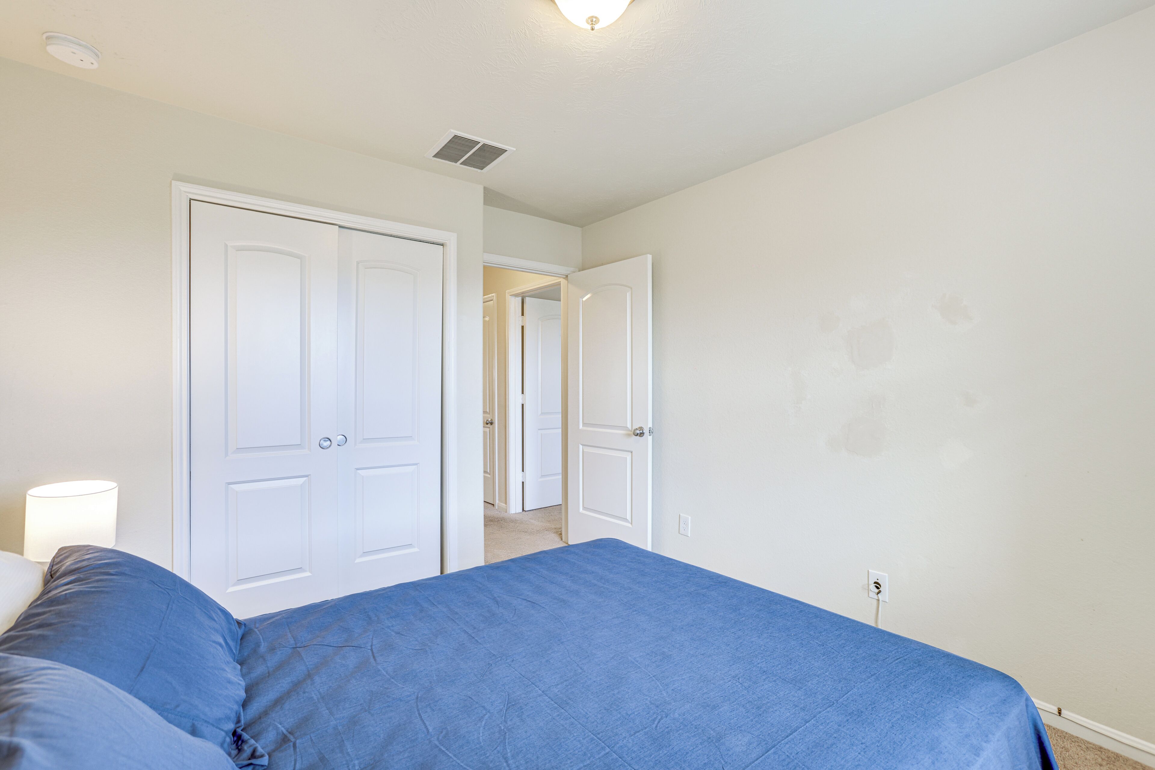 A bedroom with a bed, two doors, a light fixture, and a wall outlet.