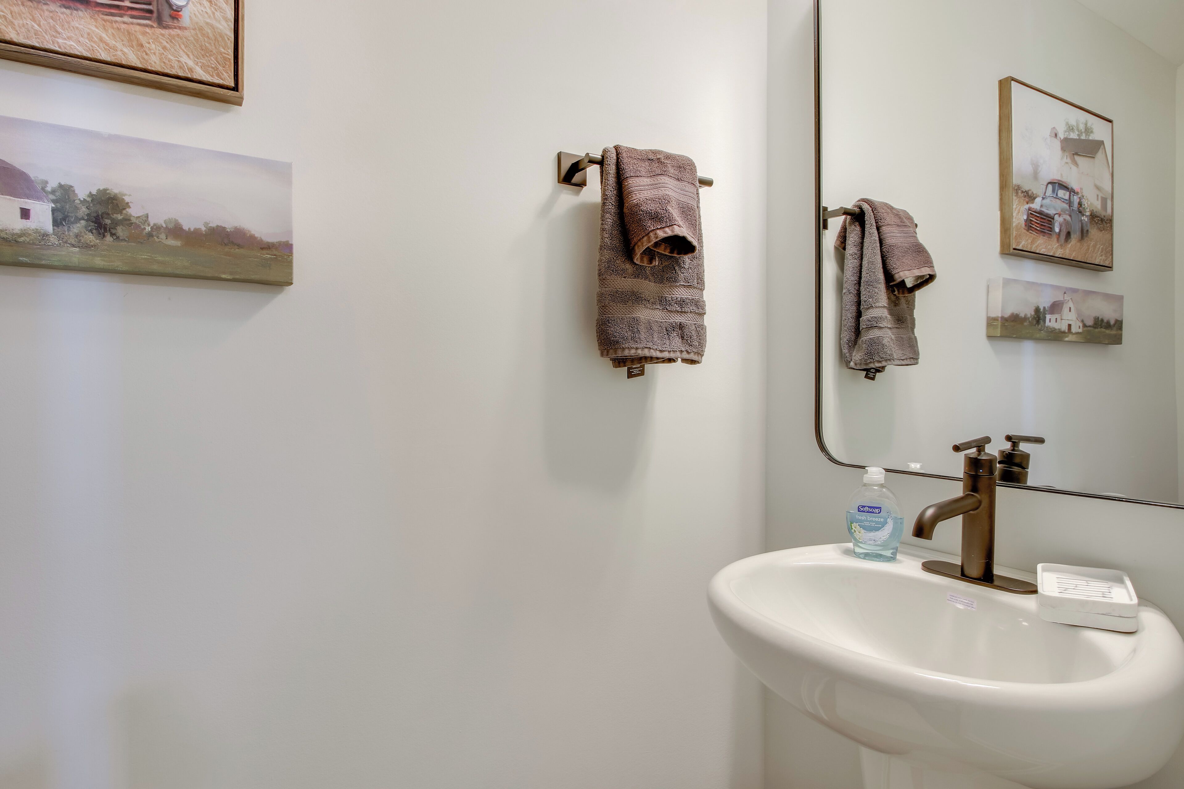A bathroom with a white sink, a mirror, and three towels hanging on a towel rack.