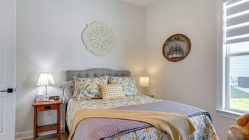 Quarto com cama, abajures, mesa de cabeceira, um objeto decorativo na parede e uma janela com persianas.