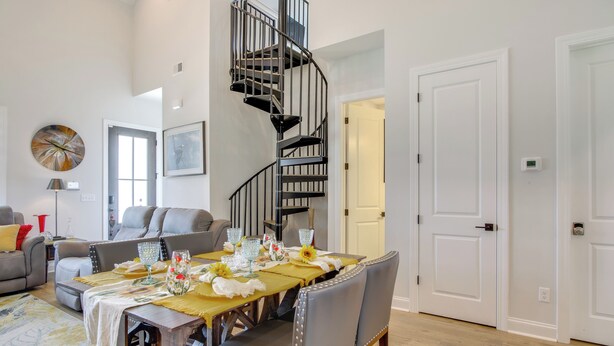 A dining area with a table set for four, a spiral staircase, and a living room with a sofa and a coffee table.