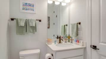 Un baño con inodoro, lavabo y espejo. Hay toallas colgadas en un perchero y artículos de aseo en la encimera del lavabo.