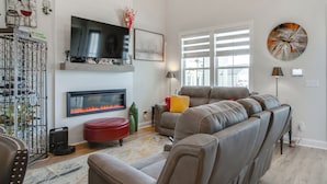 A living room with a fireplace, a large flat-screen TV, a sofa, and a red ottoman.