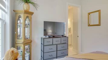 Un dormitorio con cama, cómoda con televisor, espejo y ventana con persianas.